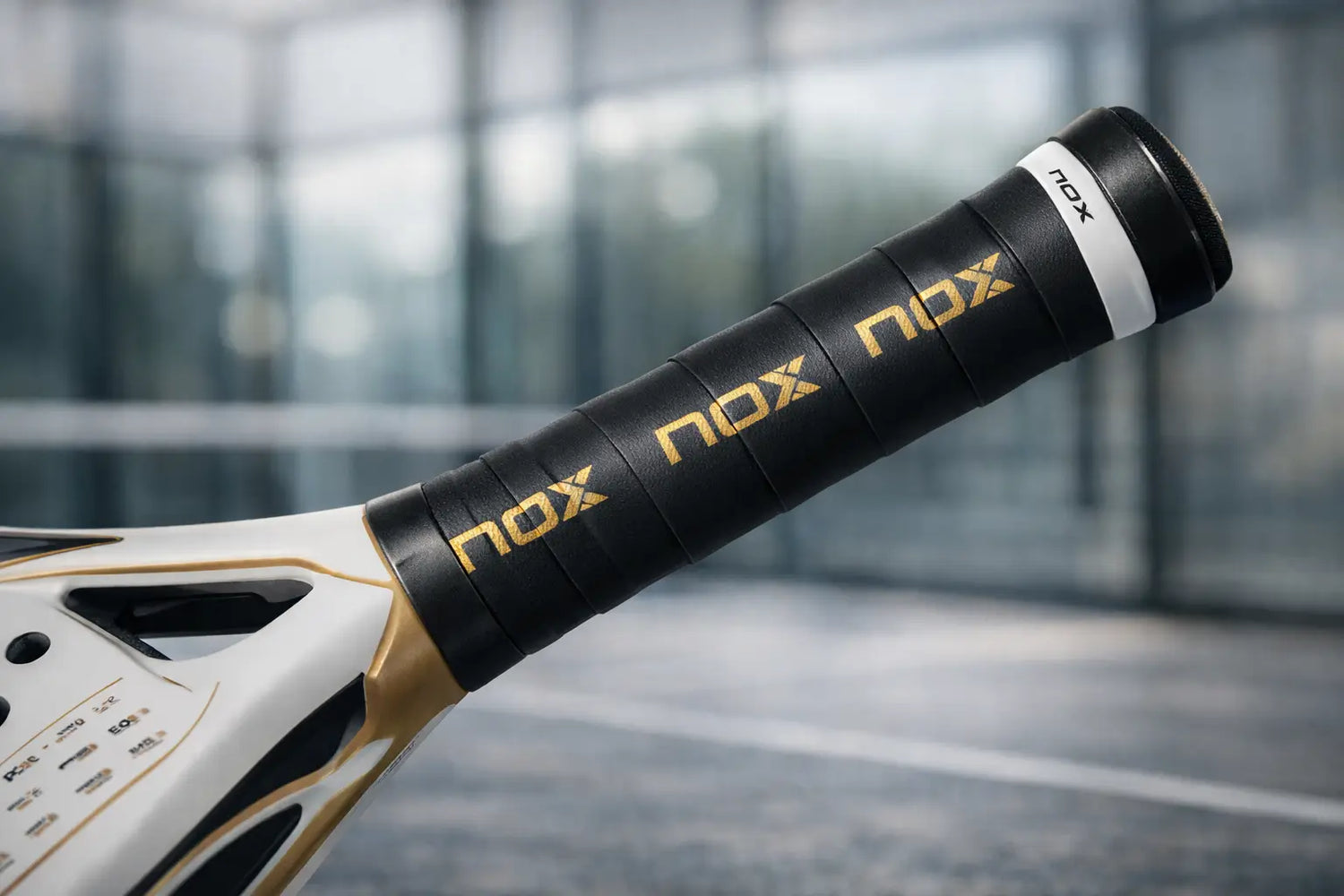 Nox overgrip on a nox tennis racket. Padel court in the background blurred. 