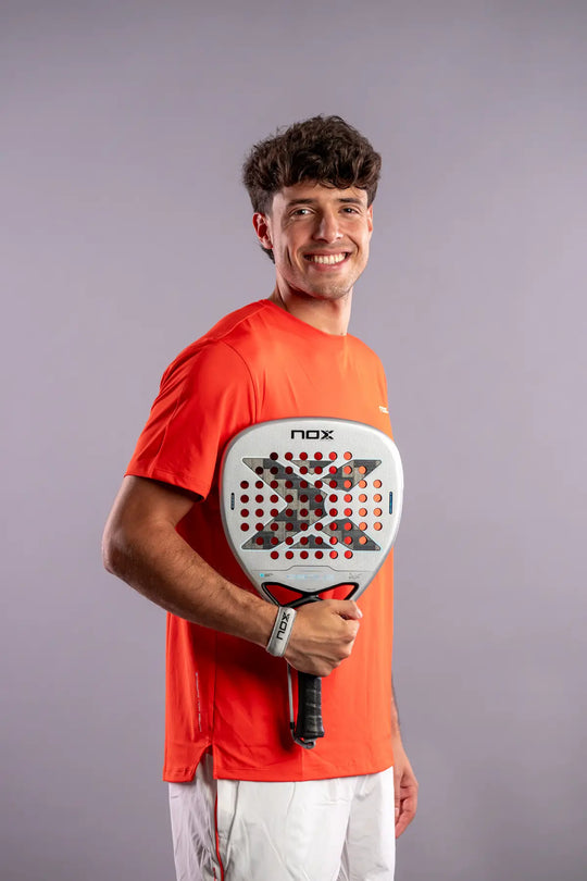 Smiling player in an orange NOX shirt holding the AT10 Genius Attack 12K Alum XTREM 2027 padel racket across his chest