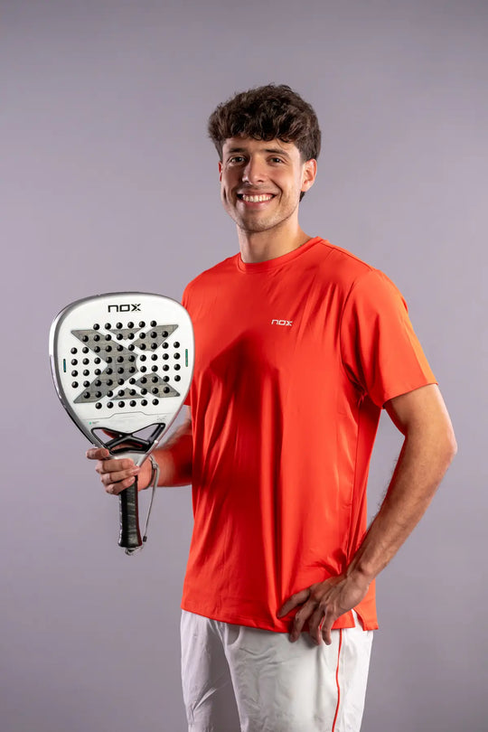 Player wearing an orange NOX shirt and holding the silver NOX AT10 Genius Attack 12K Alum XTREM 2027 padel racket