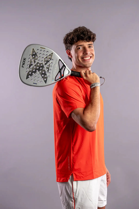 Player in an orange NOX shirt resting the AT10 Genius Attack 12K Alum XTREM 2027 padel racket on his shoulder