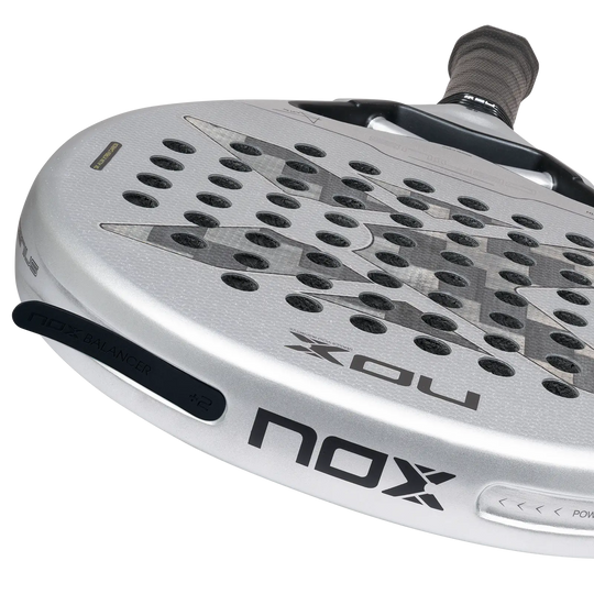 NOX Genius 12K Alum XTREM 2027 close-up showing 12K carbon face, silver frame and black NOX Balancer +2 insert