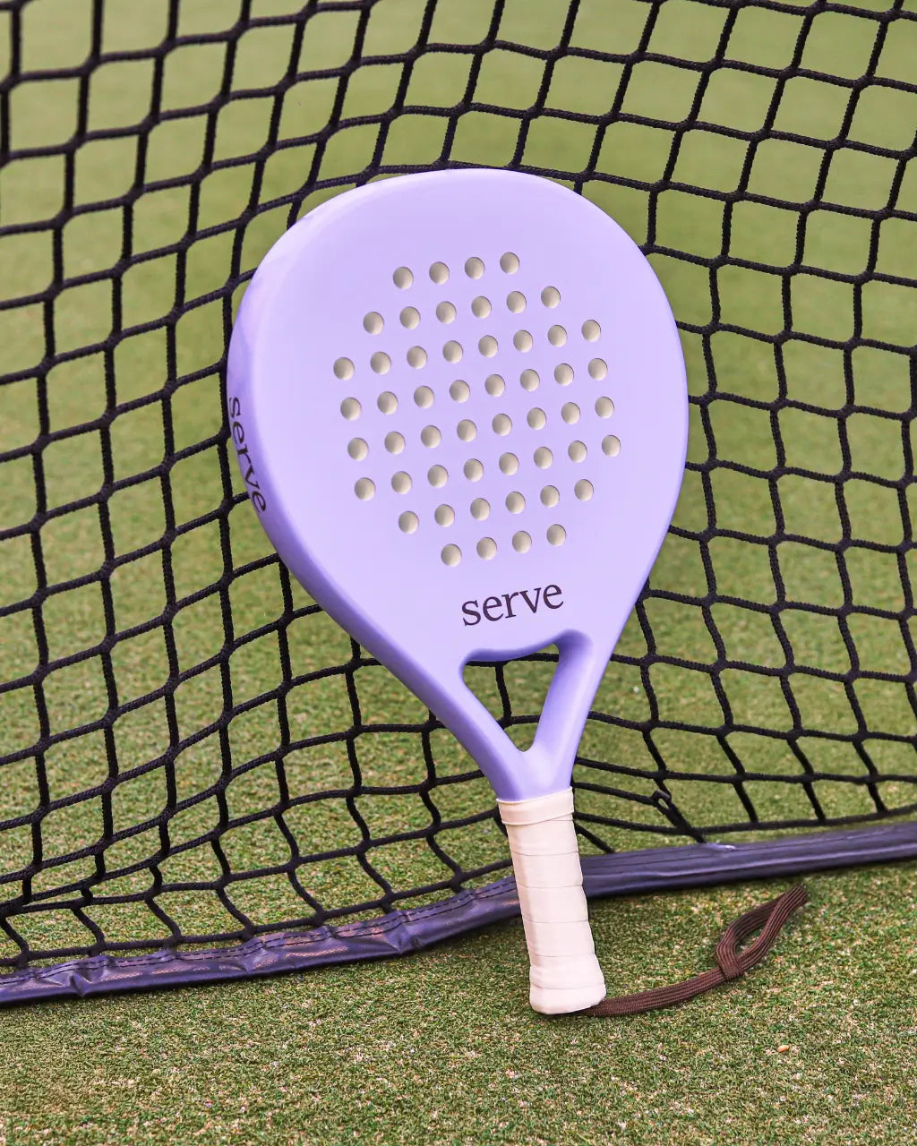 Serve womens padel racket resting against padel net on court, designed for women players